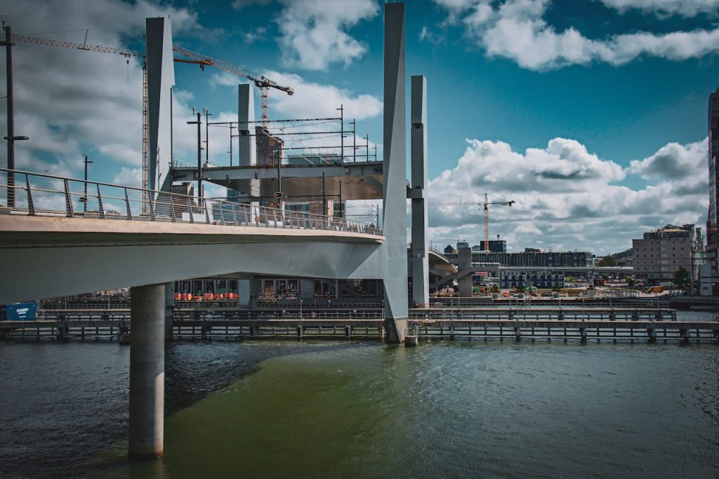A contemporary bridge over water with a cityscape in the background under a vibrant blue sky.